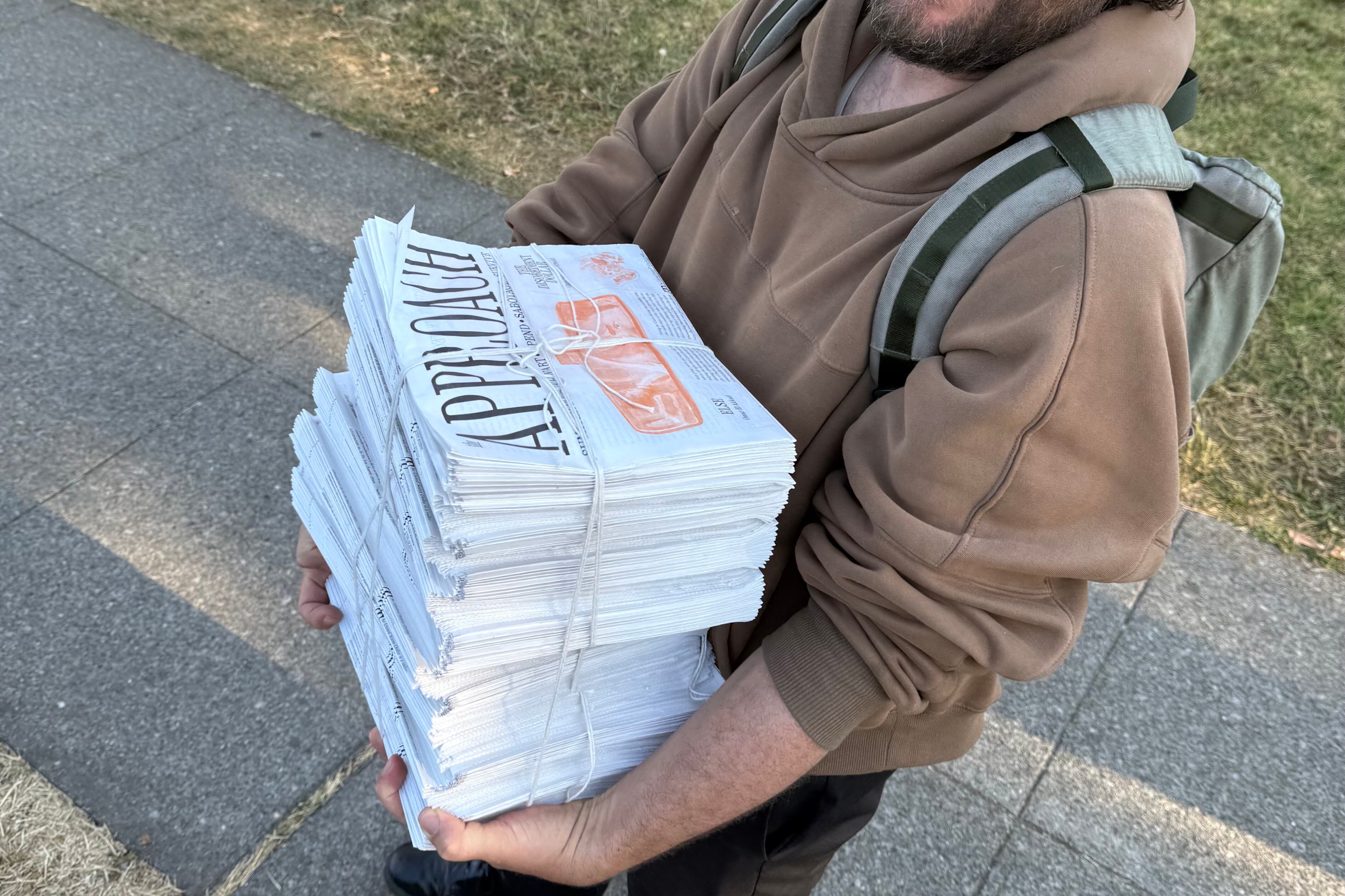 A man holds a stack of newspapers, The Approach