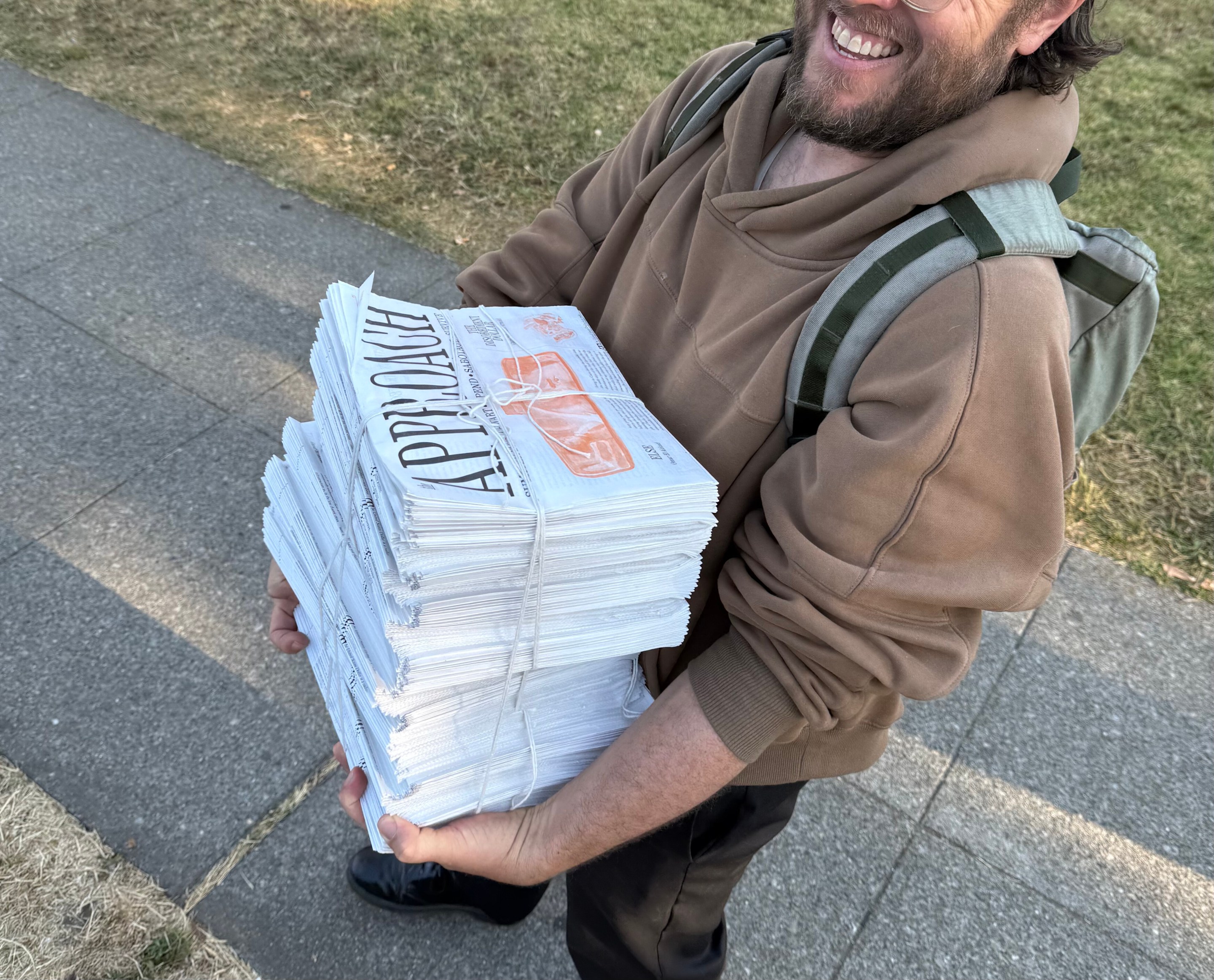 A man holds a stack of newspapers, The Approach