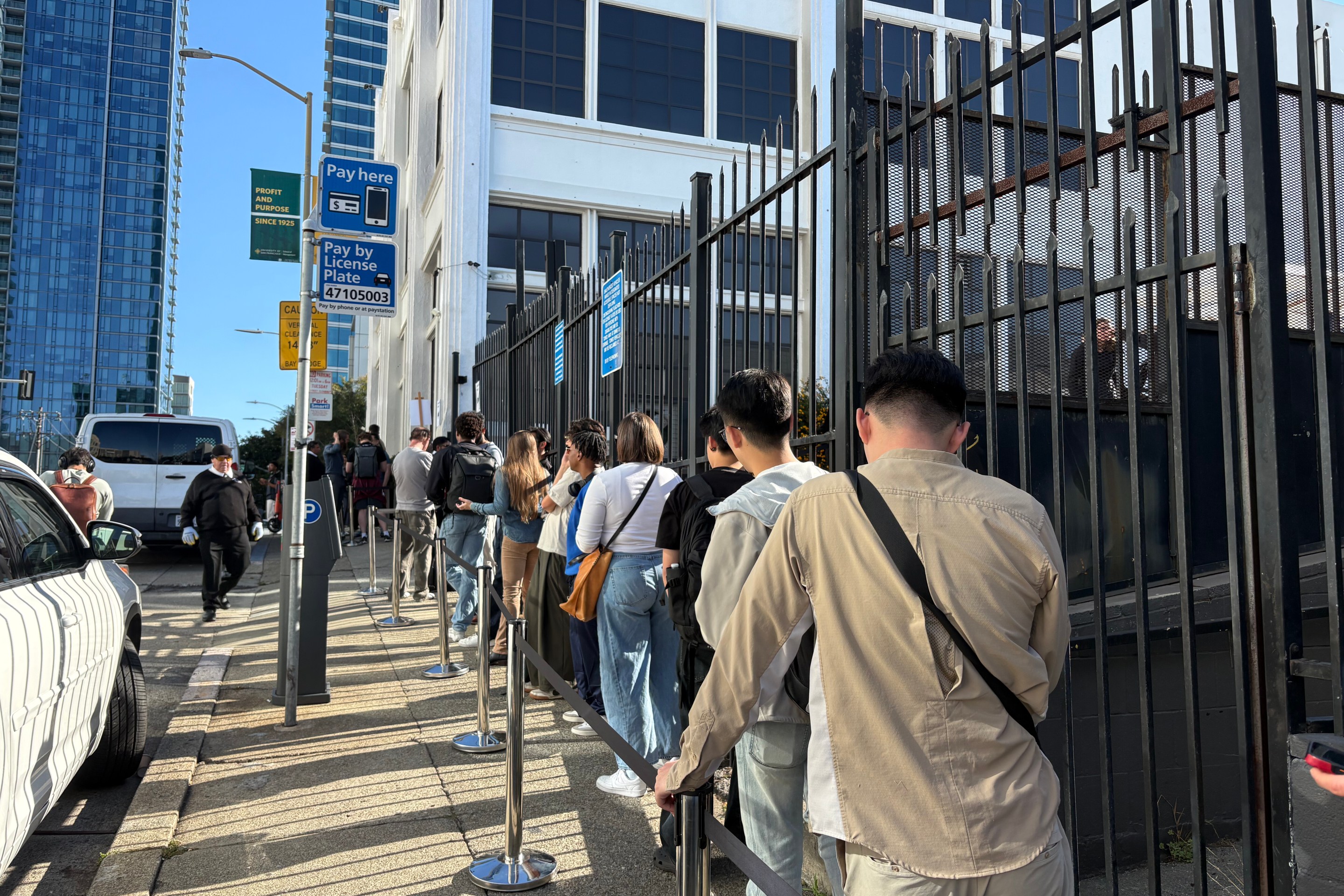 Urban street scene with line of pedestrians standing along a building and metal fencing