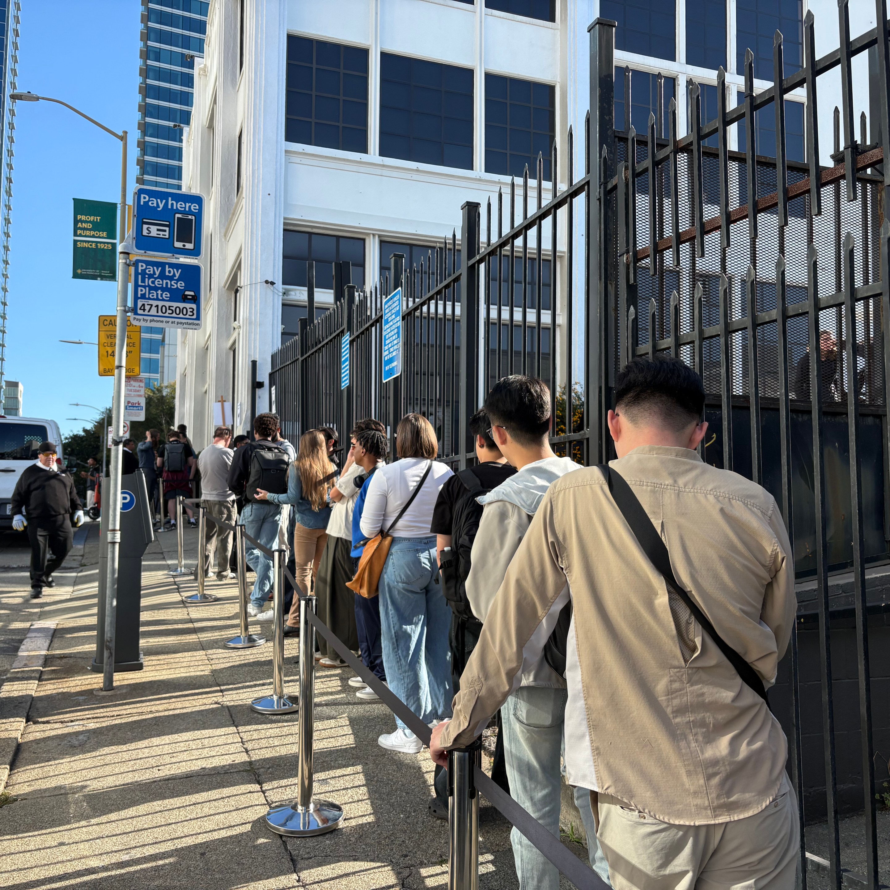 Urban street scene with line of pedestrians standing along a building and metal fencing