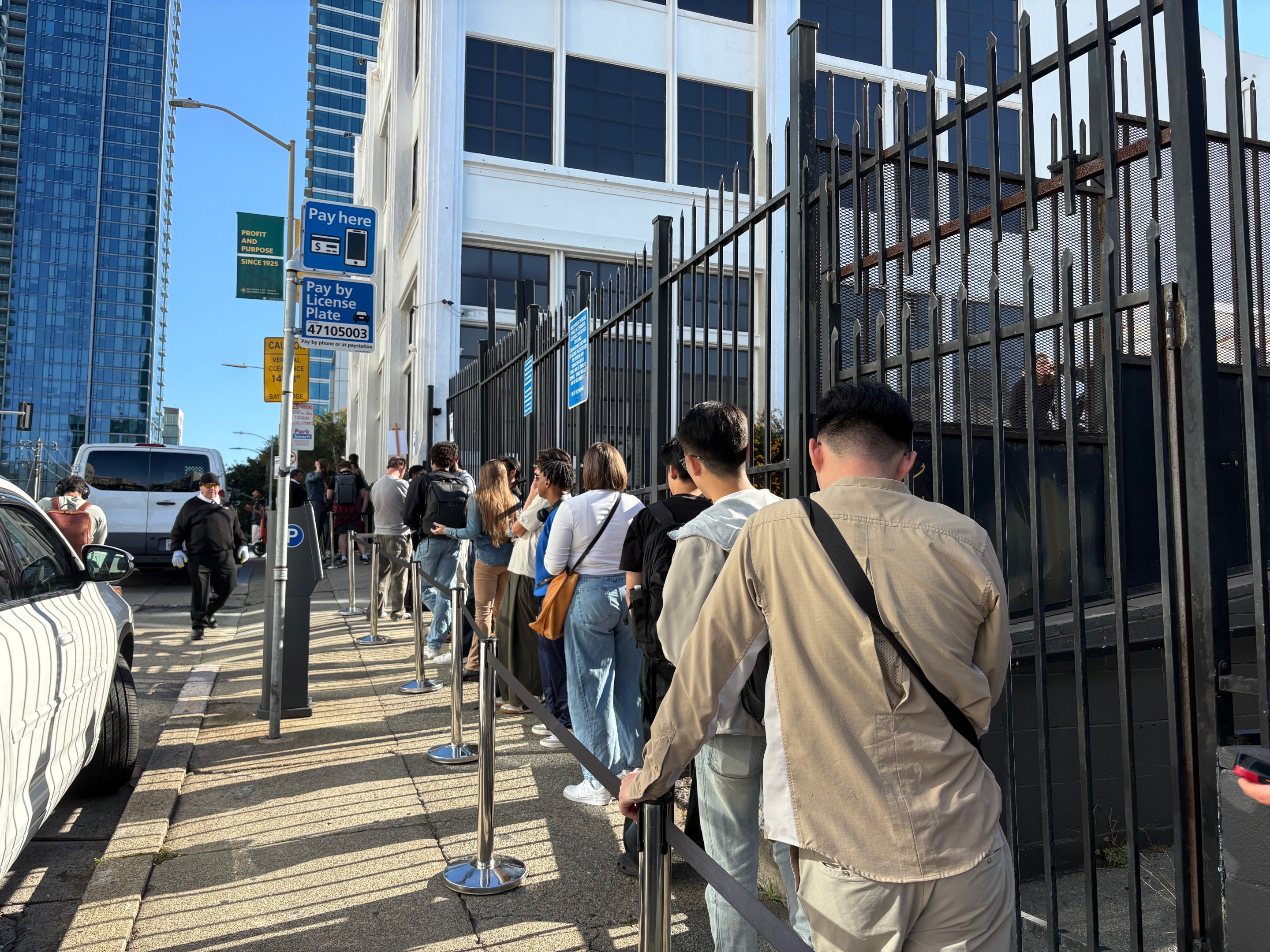 Urban street scene with line of pedestrians standing along a building and metal fencing