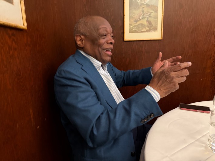Senior man in navy suit gesturing while speaking in an office setting