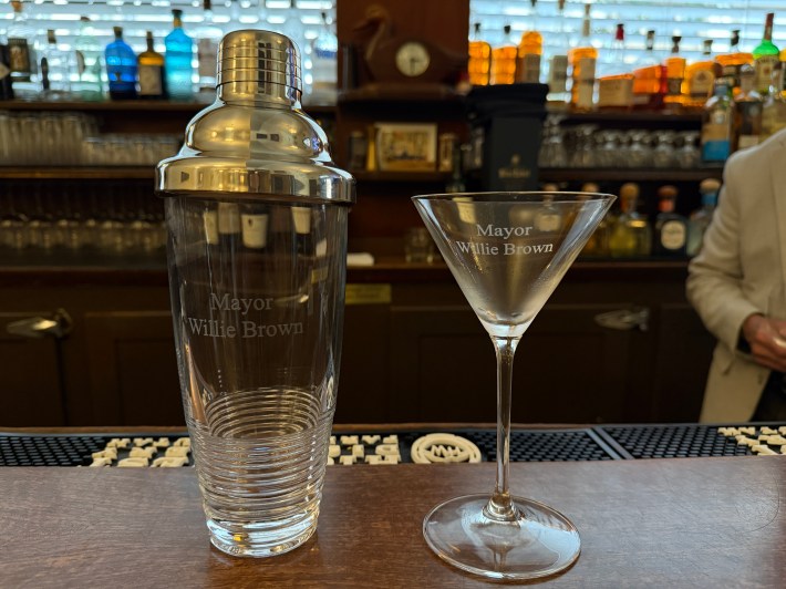 Engraved cocktail shaker and martini glass labeled Mayor Willie Brown at a bar.