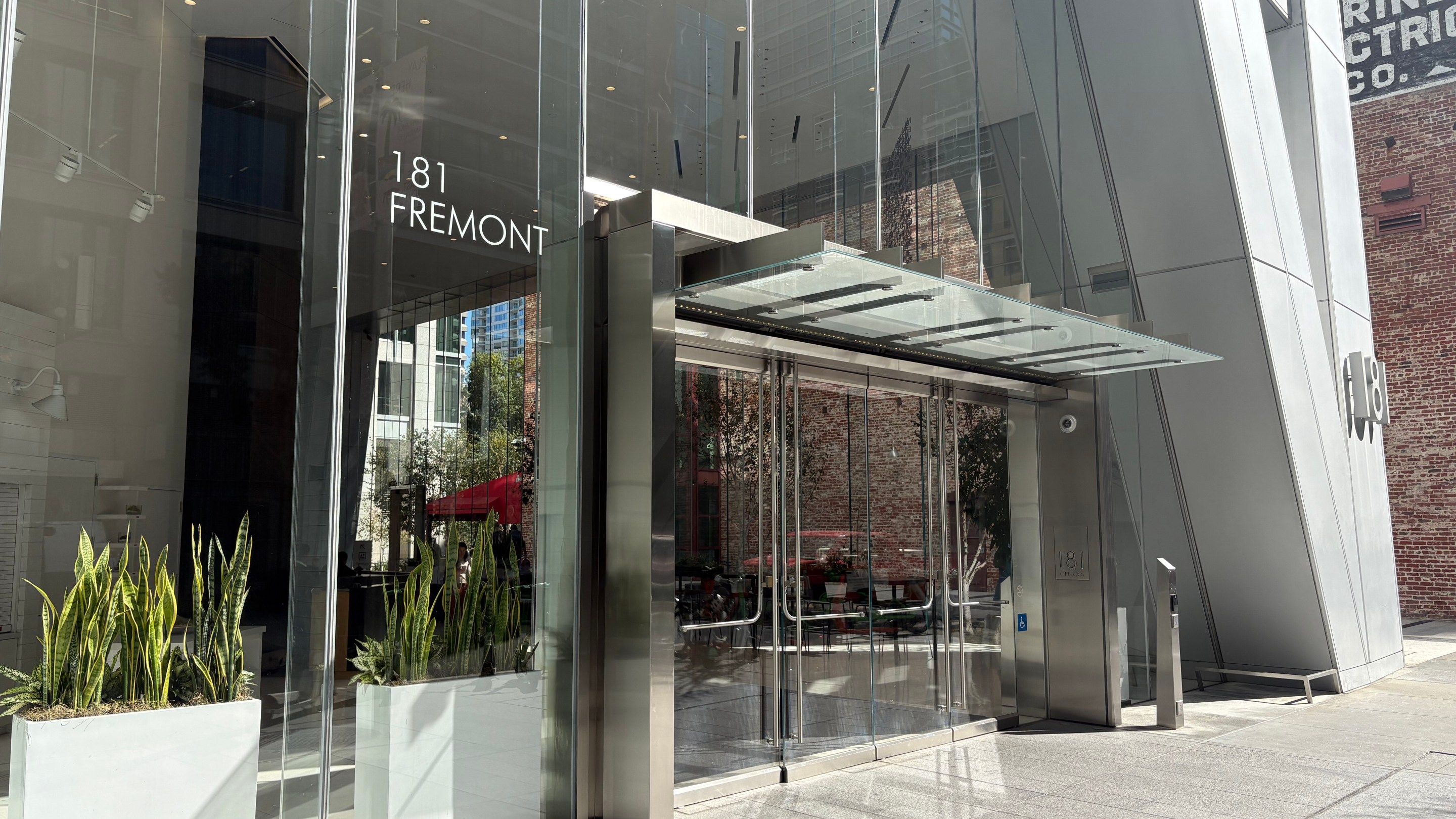 Modern glass entrance to 181 Fremont building with metal canopy and potted plants
