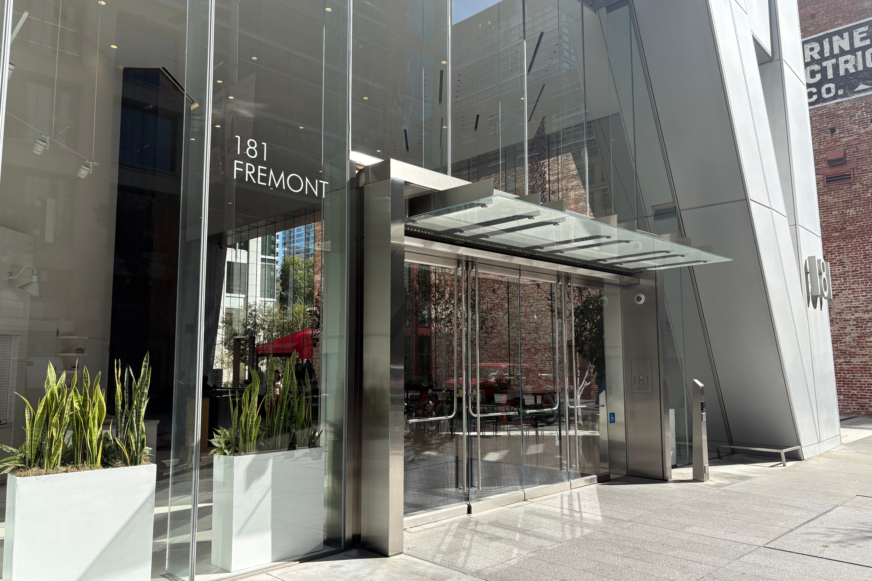 Modern glass entrance to 181 Fremont building with metal canopy and potted plants