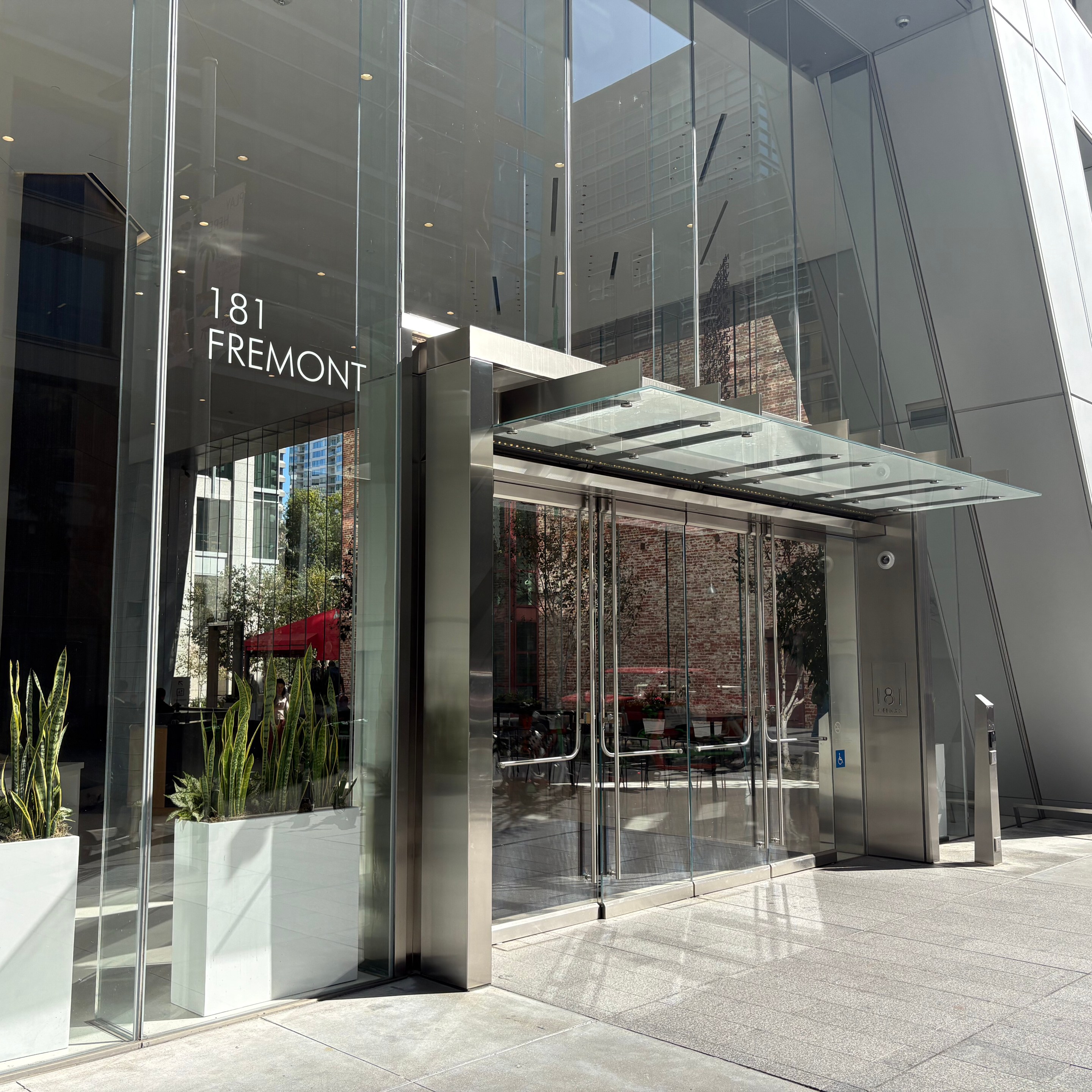 Modern glass entrance to 181 Fremont building with metal canopy and potted plants