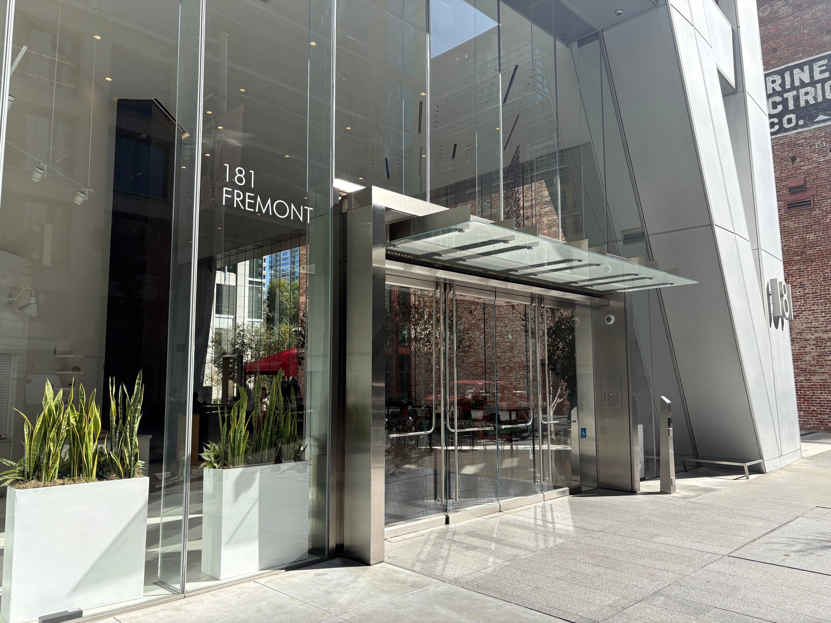 Modern glass entrance to 181 Fremont building with metal canopy and potted plants