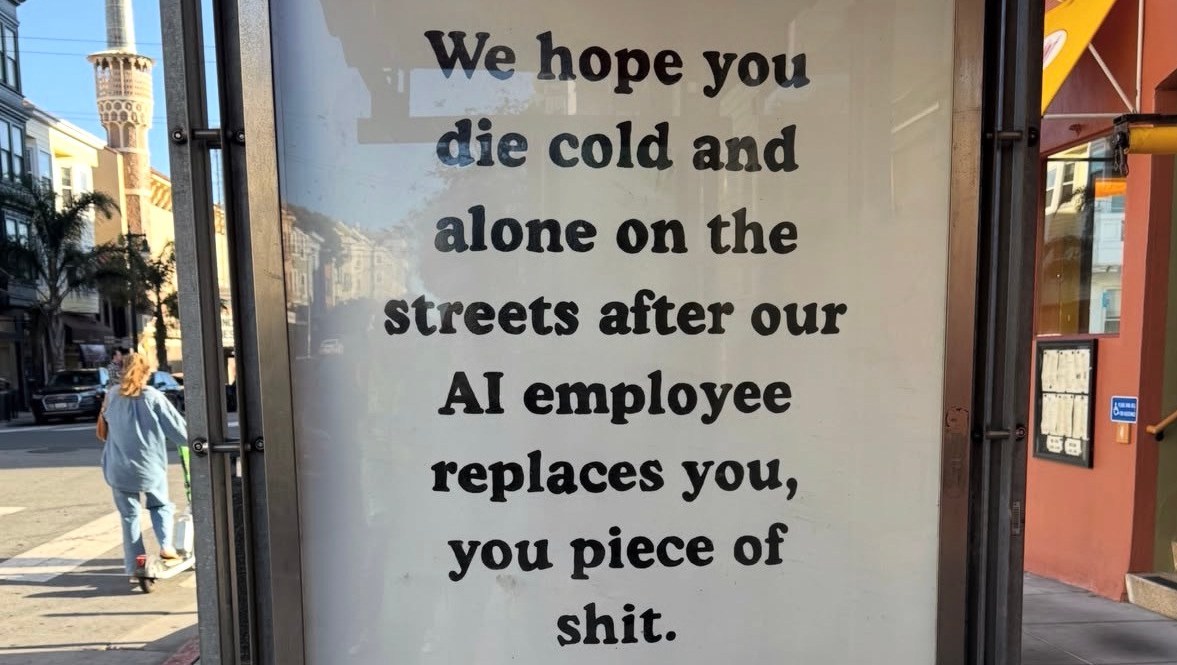 Protest sign in bus shelter criticizing AI job replacement with aggressive messaging