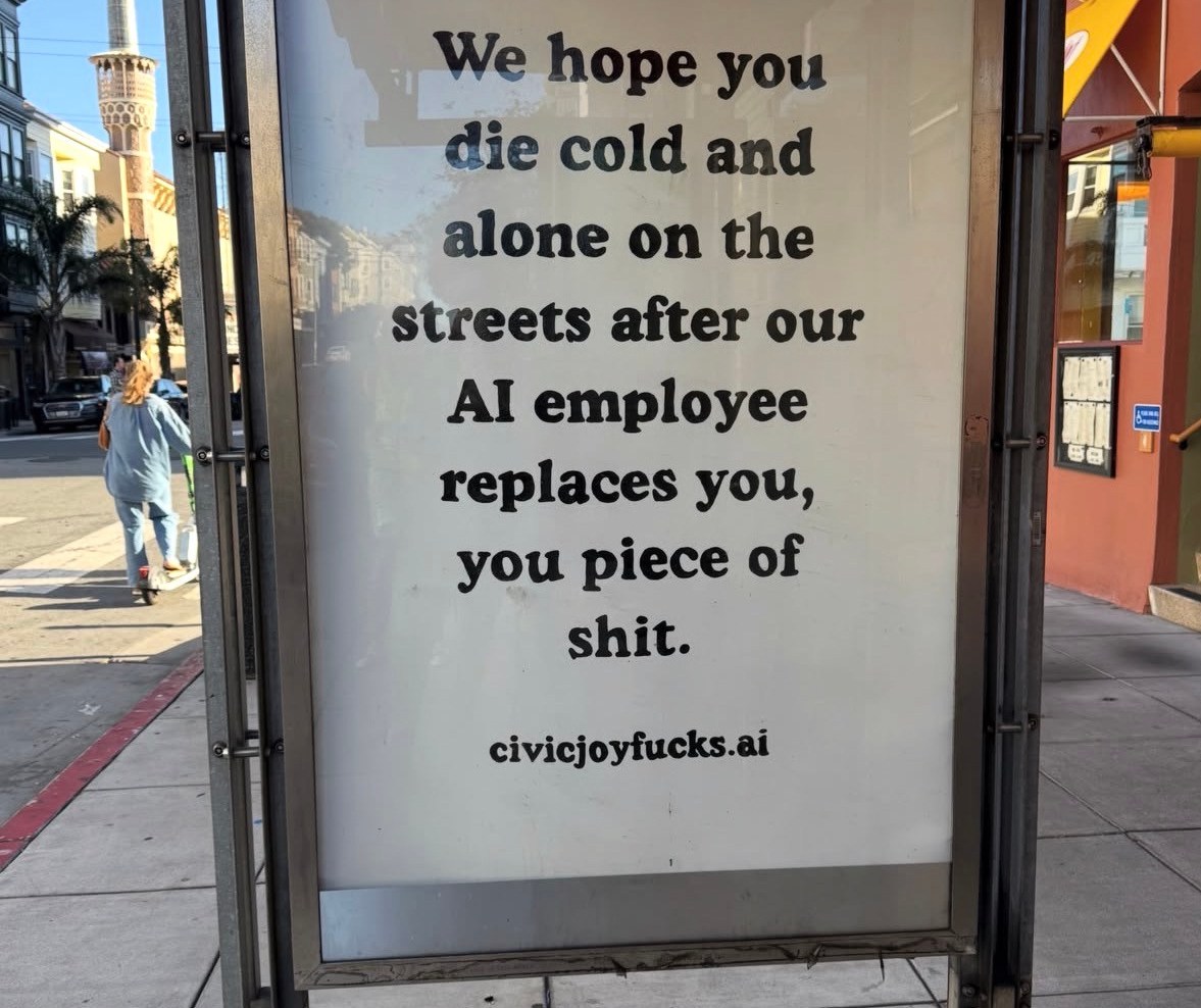 Protest sign in bus shelter criticizing AI job replacement with aggressive messaging
