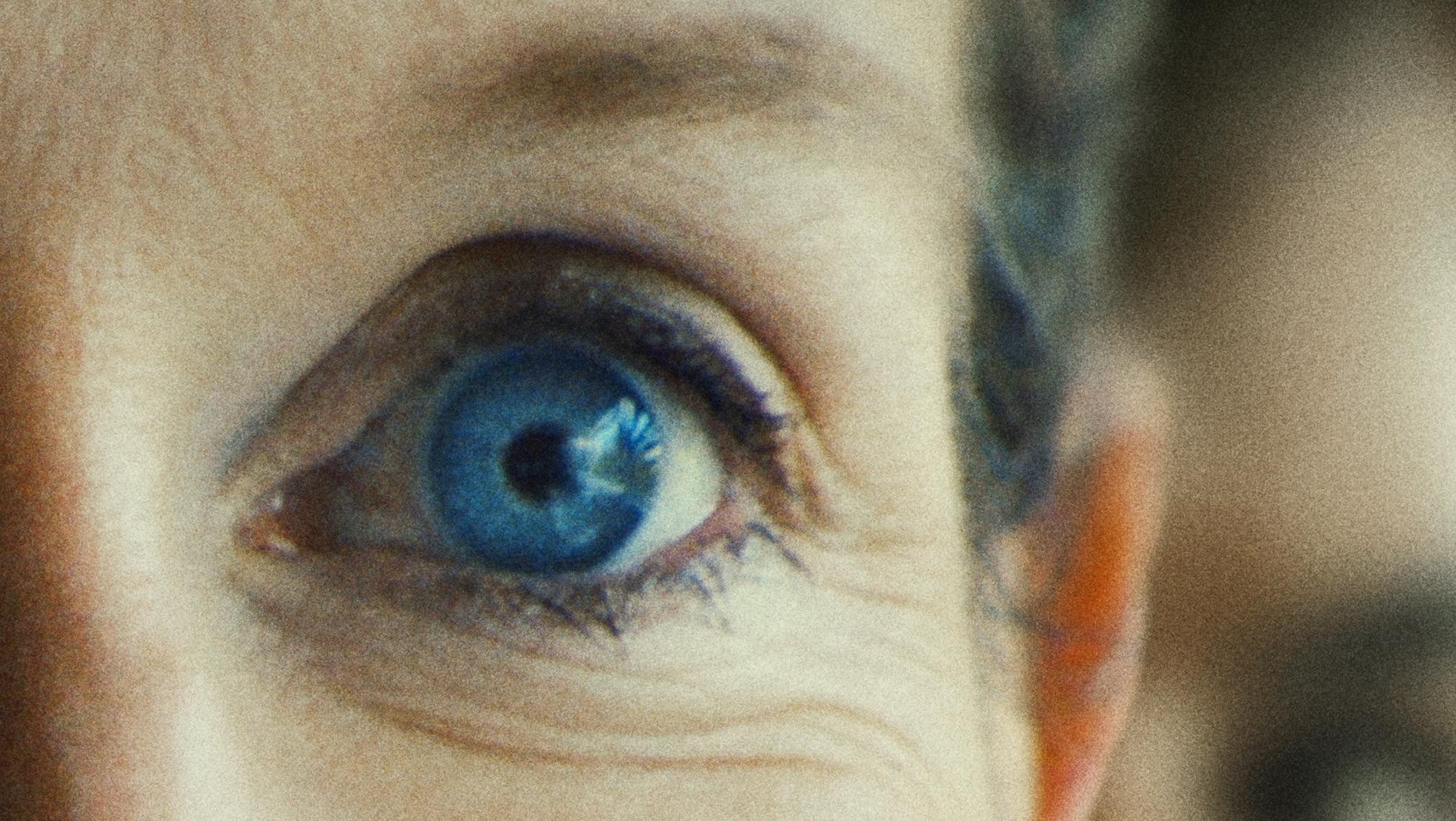 Close-up of a woman's face with bright blue eye, smiling at camera for documentary film poster